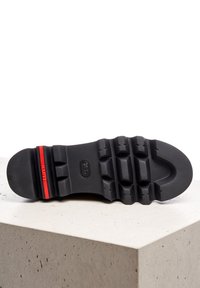 Sole nera con superficie testurizzata e scanalature profonde per una presa sicura; presenta una banda di accento rossa. Materiale di gomma liscia, forma contornata.
