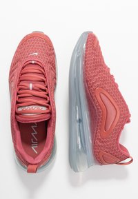 Röda atletiska skor i mesh med genomskinliga sulor med luftdämpning, utrustade med texturerad ovandel, runda skosnören och subtila märkesdetaljer.