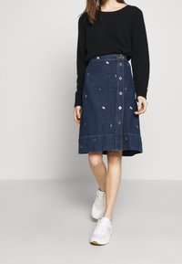 Denim skirt with embroidered motifs in various colors, featuring a front button closure, a mid-length design, and a slight flare at the hem.