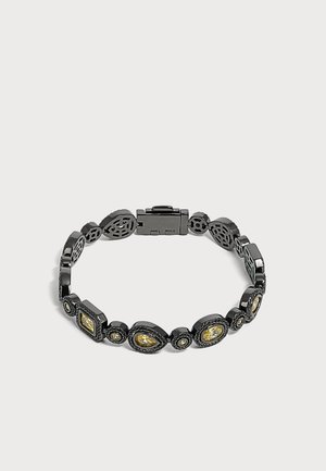 Bracelet en métal noir avec des accents de pierres précieuses jaunes de différentes formes reliées autour d'un fermoir sur un fond clair uni.