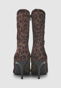 Ein Paar braune Leo-Print-Ankle-Boots mit schmalen schwarzen High Heels und einem Reißverschluss auf der Rückseite vor einem schlichten Hintergrund.