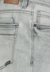 Light gray denim jeans with a faded finish, featuring multiple pockets and contrasting stitching. Includes a black brand label on the back.