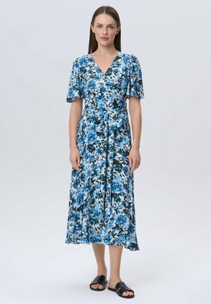 Blumenkleid mit kurzen Puffärmeln, das ein blau-weißes Blumenmuster aufweist, mit tailliertem Bund und schwingendem Rock; kombiniert mit schwarzen Sandalen.