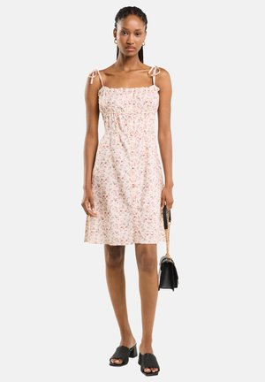 Blumen Kleid mit rosa Grundfarbe, gerafftem Taillenbund und verstellbaren Trägern. Kombiniert mit schwarzen Accessoires und strukturierten Blockabsätzen.