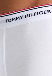 Boxeri din bumbac alb, cu un brâu texturat ce prezintă dungi roșii și bleumarin și logo-ul "TOMMY HILFIGER" afisat proeminent.