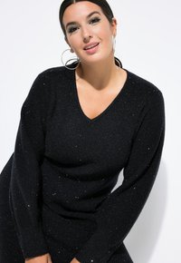 Schwarzer Langarmpullover mit V-Ausschnitt, der ein strukturiertes Strickmuster und funkelnde silberne Akzente aufweist.