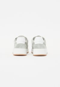 Sneakers in suede grigio chiaro con accenti bianchi e suole bianche texturizzate, dotate di una linguetta imbottita e dettaglio a linguetta sul retro.