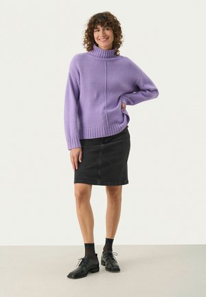 Lavender turtleneck sweater with ribbed cuffs and hem, paired with a black denim skirt. Model wears black shoes and patterned socks.