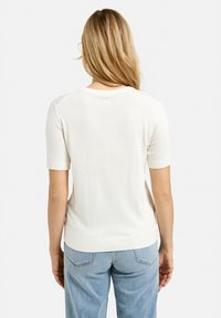 Weißes kurzärmeliges Strickoberteil mit Rundhalsausschnitt und geripptem Saum. Weiche Textur, glatte Oberfläche und minimale Design-Details.