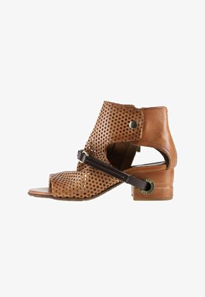 Bottine à bout ouvert en cuir marron avec partie supérieure perforée, sangle noire sur le devant, et petit talon bloc avec détail métallique.