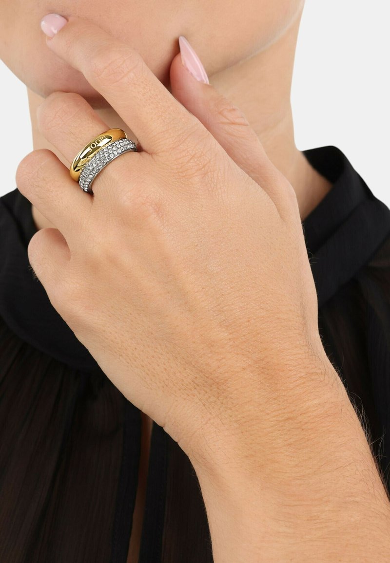 Anelli d'oro e d'argento impilati su una mano, con una fascia d'oro liscia e una fascia d'argento decorata con pietre trasparenti scintillanti.