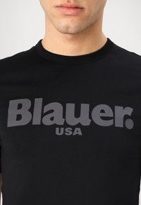 T-shirt nera in cotone con un grande logo grigio stampato "Blauer. USA" sulla parte anteriore. Collo tondo classico e maniche corte.