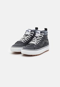 Höga sneakers gjorda av mörk canvas med vita snören och en gummisula. Har en rutigt foder och kontrasterande sömnadsdetaljer.