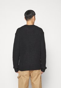 Czarny sweter z dzianiny o grubej, teksturowanej tkaninie i ribbowe kołnierzu. Opuszczone ramiona i długie rękawy tworzą luźny krój.