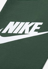 Tejido verde con un destacado logo blanco de Nike y un swoosh blanco en ángulo, con una textura suave y un diseño elegante y moderno.