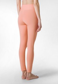 Perzikkleurige leggings van rekbaar materiaal met een hoge tailleband, een aansluitende pasvorm en een gladde textuur. Heeft een naadloos ontwerp.