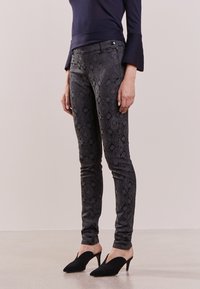 Smal jeans i svart strukturerat tyg med ett subtilt blommönster, ihop med svarta klacktofflor. Mörk tröja med trumpetärmar.