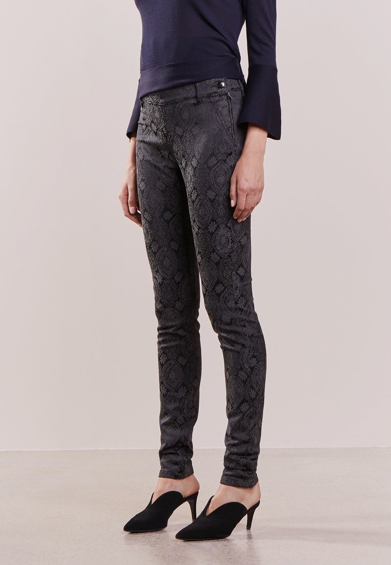 Smal jeans i svart strukturerat tyg med ett subtilt blommönster, ihop med svarta klacktofflor. Mörk tröja med trumpetärmar.