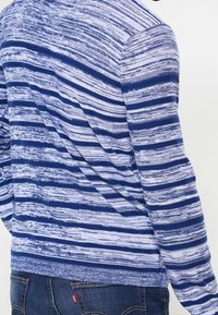 Blå och vit randig långärmad tröja med texturerad stickning. Har en rundad halsringning och ribbade manschetter och nederkant.