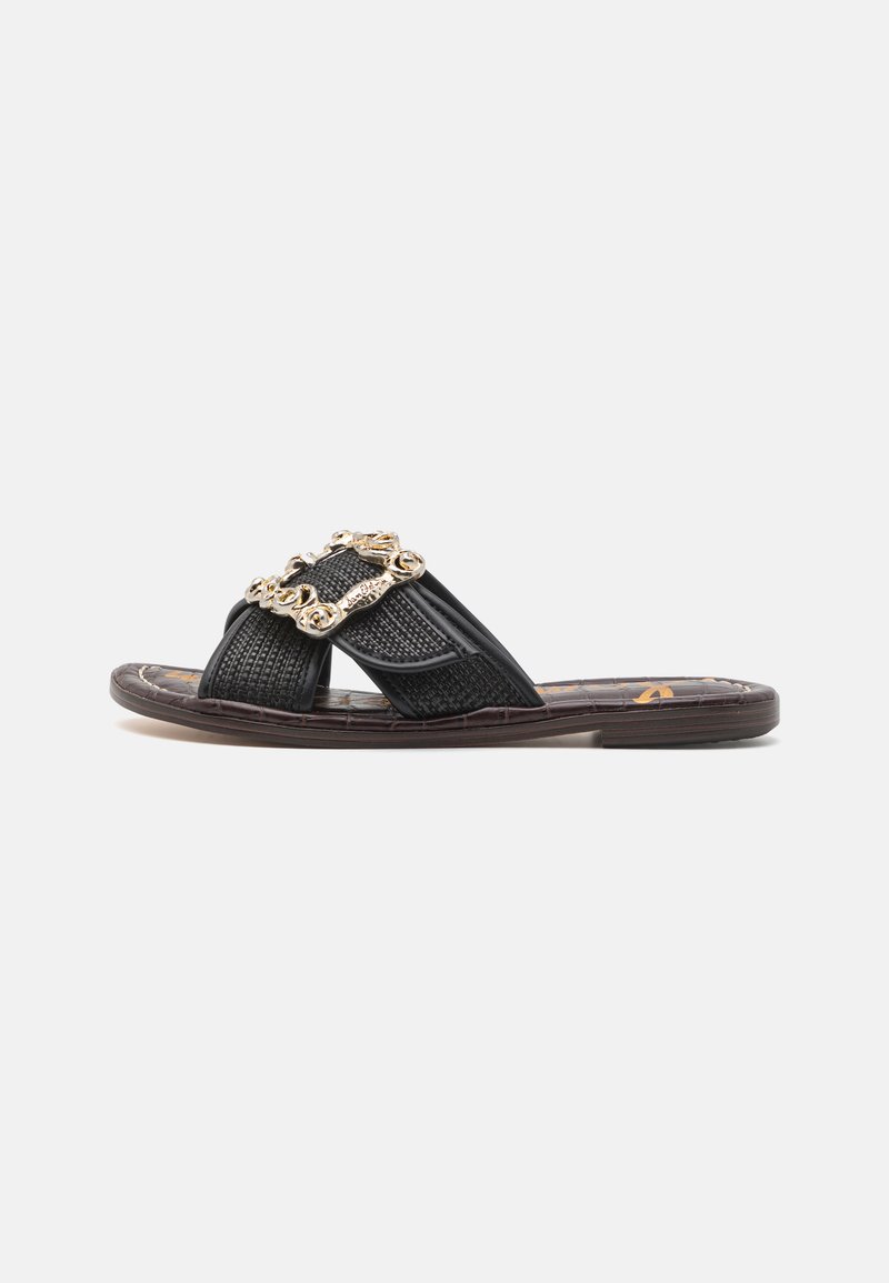 Black slide sandal with crisscross straps, textured fabric, and a decorative gold-tone buckle. Flat sole, understated design.