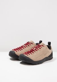 Beige suede shoes with black rubber soles and red laces. Features a streamlined design and pull tabs at the heel for easy wear.