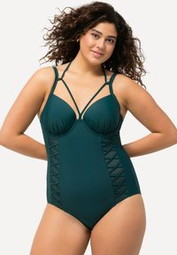 Maillot de bain une pièce teal avec des bonnets, des bretelles croisées et des panneaux latéraux en mesh avec un motif géométrique. Tissu lisse avec un léger éclat.