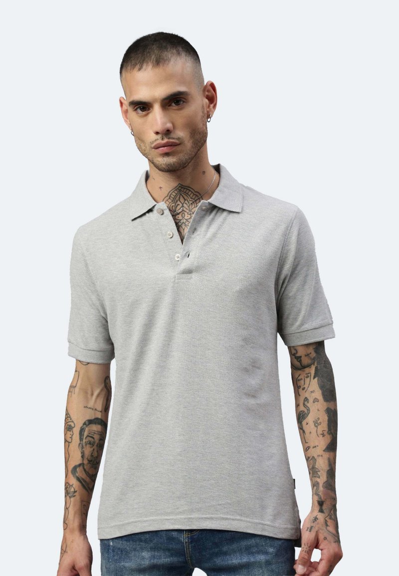 Graues Poloshirt mit kurzen Ärmeln und einem Knopfkragen. Der Stoff hat ein strukturiertes Muster. Das Modell hat sichtbare Tätowierungen an den Armen.