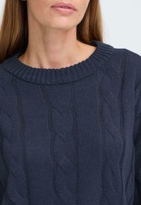 Maglione navy a maglia cable, con scollatura a costine e motivi testurizzati. Dettagli includono una morbida trama tessuta e un design rilassato.