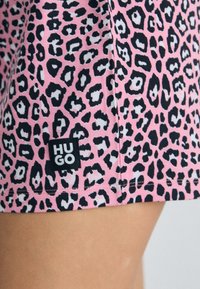 Ružové šortky s leopardím vzorom a čiernymi a bielymi akcentmi. Obsahujú čiernu nášivku so slovom "HUGO" blízko švu. Vyrobené z mäkkej látky.