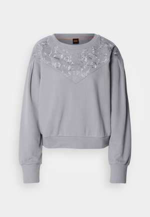 Felpa grigia chiaro con ricami floreali sulla spalla, collo rotondo e polsini elasticizzati. Ha una vestibilità rilassata e una texture morbida.