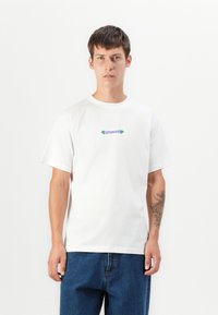 Weißes Baumwoll-T-Shirt mit kurzen Ärmeln, das ein farbenfrohes, besticktes "LETPOMANIC"-Textdesign auf der Brust trägt. Lockerer Schnitt.