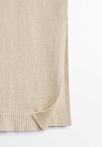 Beige gebreide trui met een geribde zoom en zijsplitten. Zachte textuur, lange mouwen en een klassiek ronde halsontwerp.