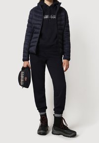 Granatowa kurtka puchowa na czarnej bluzie z kapturem, w zestawie z dopasowanymi dresami i czarnymi wodoodpornymi butami. Akcesorium: mała czarna torba z detalem logo.