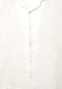Camicia bianca con bottoni, realizzata in cotone testurizzato, caratterizzata da un delicato motivo a griglia e da un colletto con cinque bottoni sul davanti.