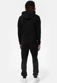 Zwarte capuchontrui en bijpassende joggingshort, gemaakt van zachte stof. Bevat elastische boorden en een tailleband, met een achterzak op de joggingshort.