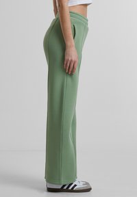 Lichtgroene sweatpants met een relaxte pasvorm, zijzakken en een brede elastische tailleband, gemaakt van zachte stof. Gestyled met witte sneakers.