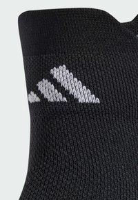 Chaussette de sport noire avec une texture côtelée et un logo trois rayures brodé blanc sur le côté.