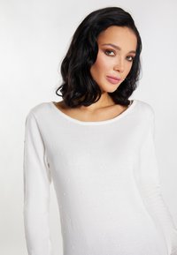 Pulover alb cu mâneci lungi, având un decolteu rotund și modele texturate sub formă de puncte pe întreaga țesătură. Material moale tricotat, cu un finisaj neted.