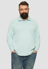 Jasnoniebieska koszula polo z długim rękawem i kołnierzykiem, wykonana z teksturowanej tkaniny bawełnianej, zestawiona z niebieskimi dżinsami. Prosty fason, bez widocznych wzorów czy akcentów.