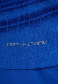 Tissu bleu texturé avec de petites perforations, présentant le texte réfléchissant "DRI-FIT ADV" imprimé sur la surface.