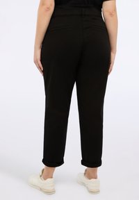 Pantaloni da donna neri, a sigaretta, con chiusura a bottone e zip, vita elastica, tasche posteriori e orli arrotolati, realizzati in tessuto morbido.