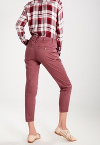 Light pink cropped pants feature a tailored fit, with a smooth texture and back pockets. Paired with a red and white plaid shirt.