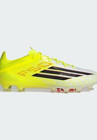 Κίτρινο-λαϊμ ποδοσφαιρικό παπούτσι με υφασμάτινο ανώτερο μέρος, μαύρες λεπτομέρειες και ελαφρύ πέλμα με διαφανείς τάπες για πρόσφυση.