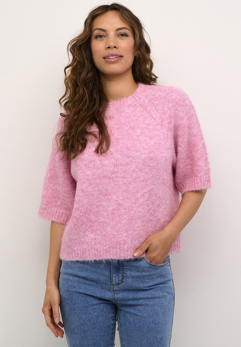 Maglione rosa, morbido e lavorato a maglia con maniche corte e larghe e un collo rotondo. Indossato con jeans blu, dal taglio rilassato.