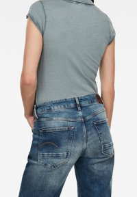 Polo de color azul claro con mangas cortas, combinado con unos vaqueros de denim azul oscuro que tienen dos bolsillos traseros y costuras en contraste.