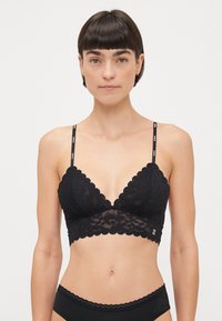 Black lace bralette featuring a scalloped edge, triangular cups, and thin adjustable straps with logo accents. Soft, textured fabric.