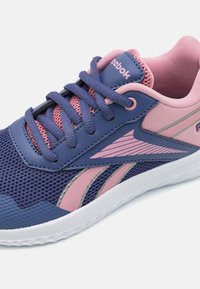 Scarpa sportiva viola e rosa con tomaia in rete, punta rotonda, suola in gomma e logo Reebok. Presenta dettagli testurizzati e righe a contrasto.