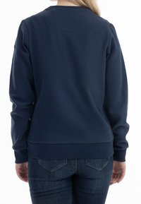 Felpa blu navy con scollo a girocollo e polsini a costine. Realizzata in un tessuto liscio e elastico. Indossata con jeans in denim scuro.