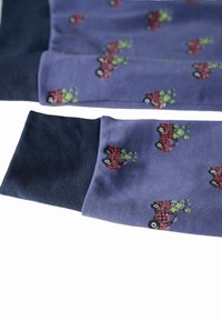 Maniche in tessuto blu con polsini neri, decorate con un motivo di auto vintage rosse che trasportano piante verdi.