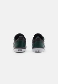 Zapatillas de cuero verde con acentos negros, diseño de corte bajo, suelas de goma blanca, con un logo en el talón y una superposición de textil.
